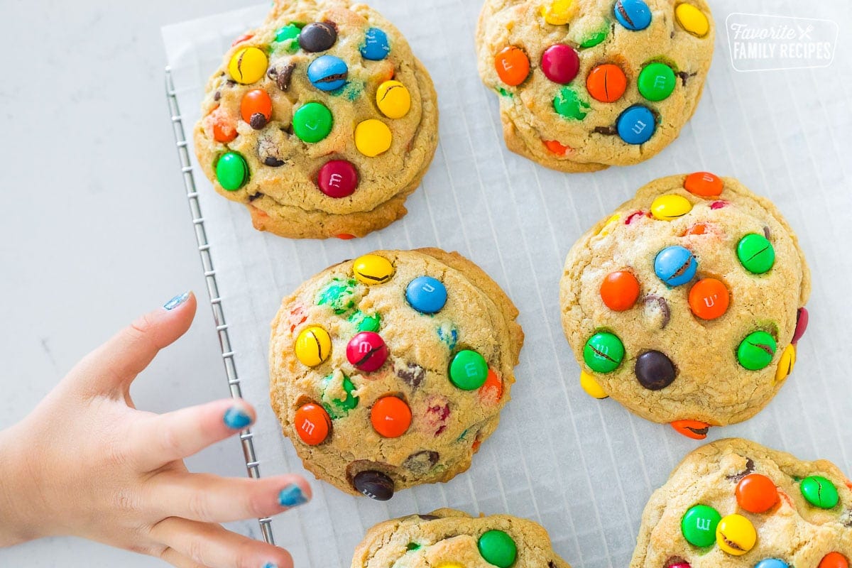 M&M cookies on a cooling rack with a child's hand reaching for a cookie