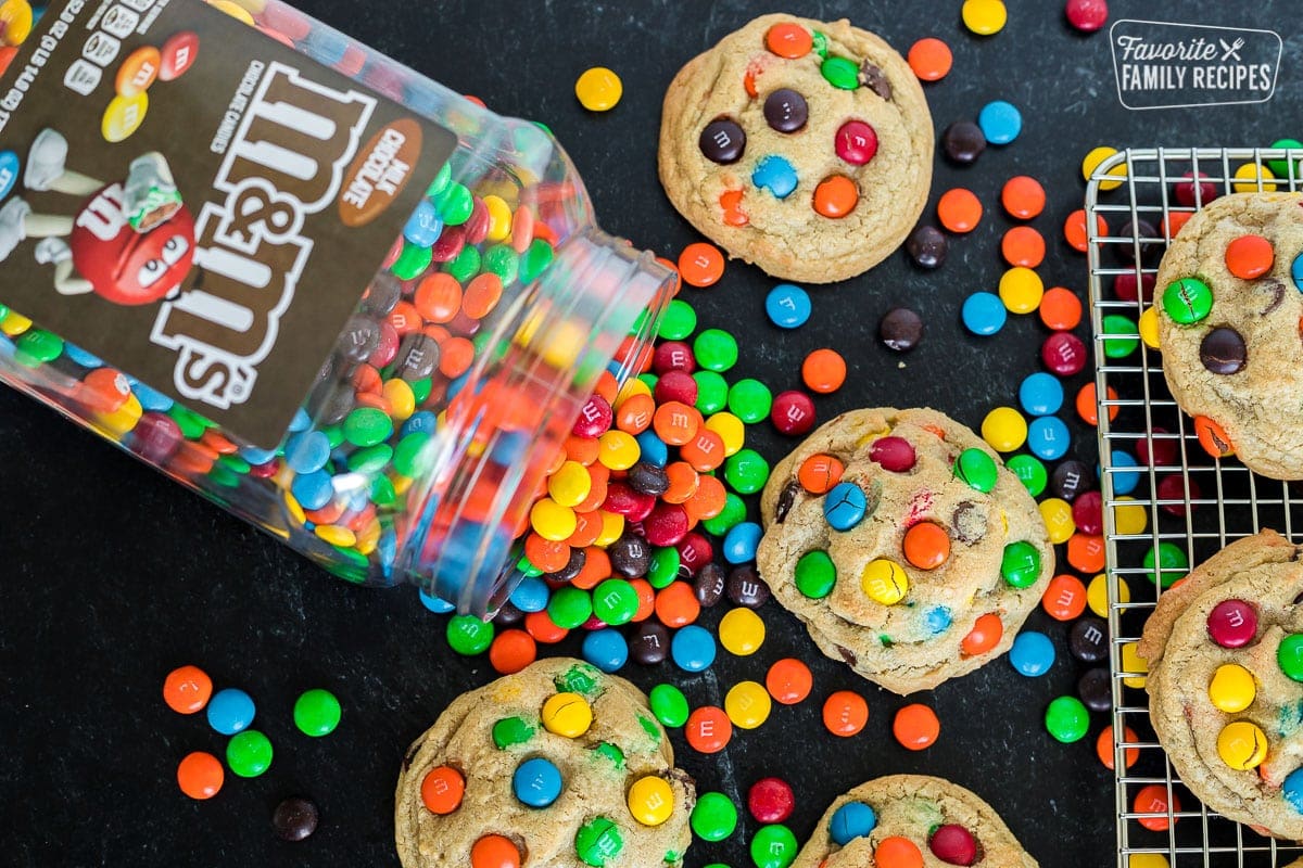 M&M cookies on a cooling rack and on a table top next to a canister of M&M candies