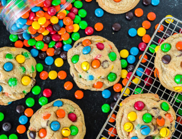 M&M cookies on a cooling rack and on a table top next to a canister of M&M candies