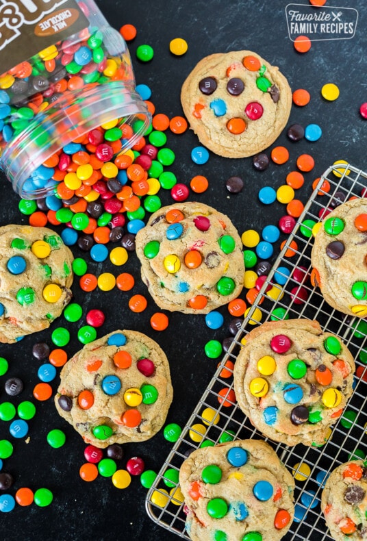 M&M cookies on a cooling rack and on a table top next to a canister of M&M candies