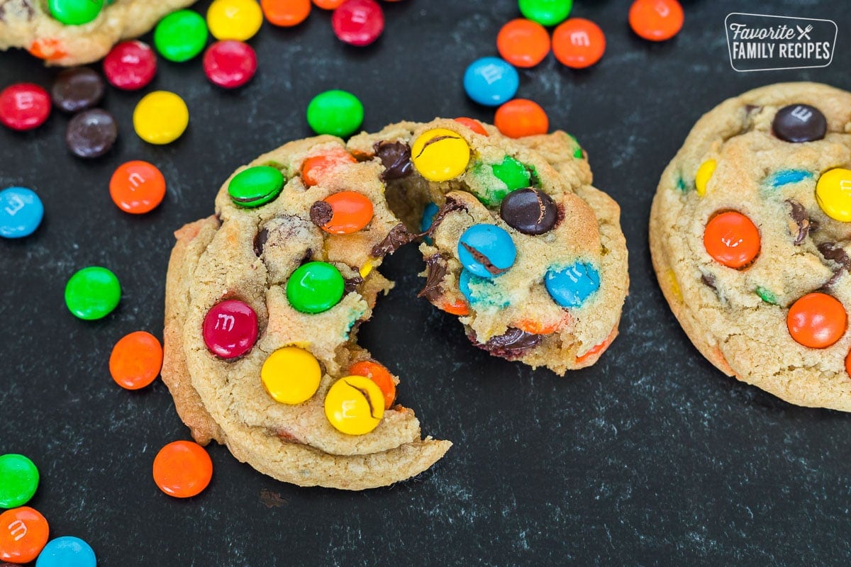 An M&M cookie on a table top that has been pulled apart to show melted chocolate inside