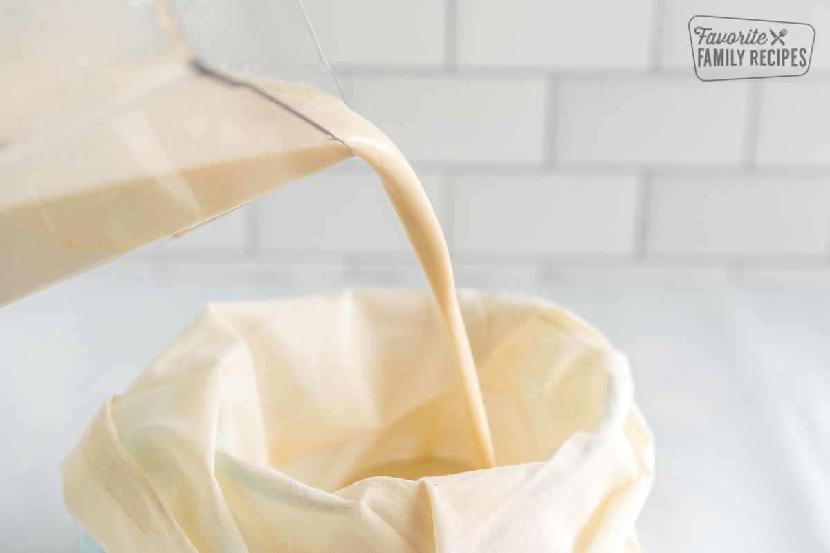 Oat milk being poured from a blender into a nut milk bag.