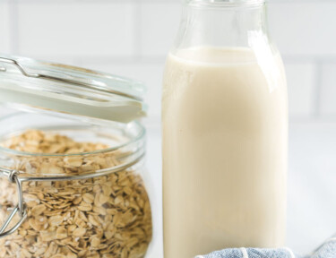 A glass of oat milk next to a container of oats