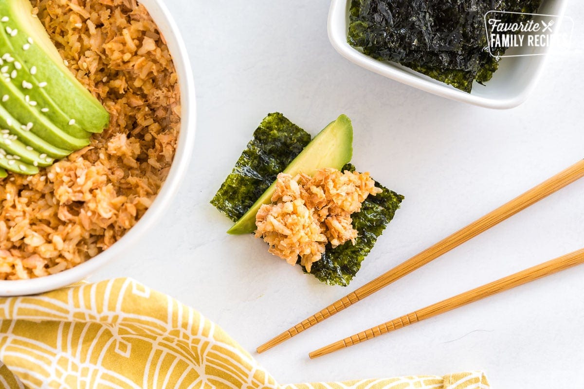 A seaweed snack topped with a slice of avocado and some salmon rice