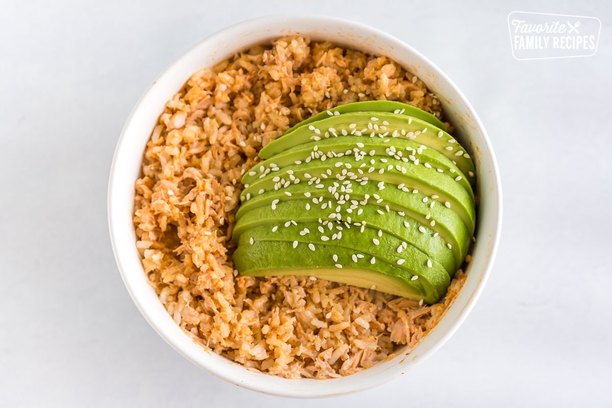 Salmon and rice topped with sauce and sliced avocado and sesame seeds