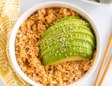 Salmon and rice in a bowl topped with sauce and sliced avocado and sesame seeds