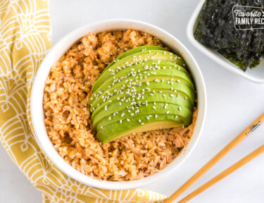 Salmon and rice in a bowl topped with sauce and sliced avocado and sesame seeds