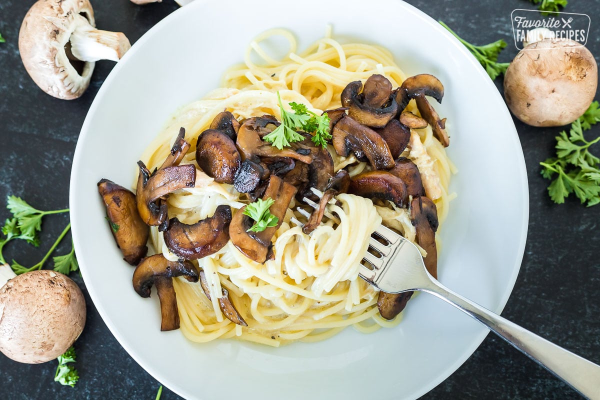 A bowl of pasta with sautéed mushrooms over the top