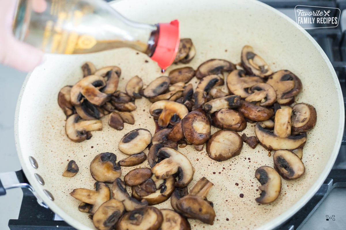Sautéed mushrooms in a frying pan with soy sauce being poured over the top