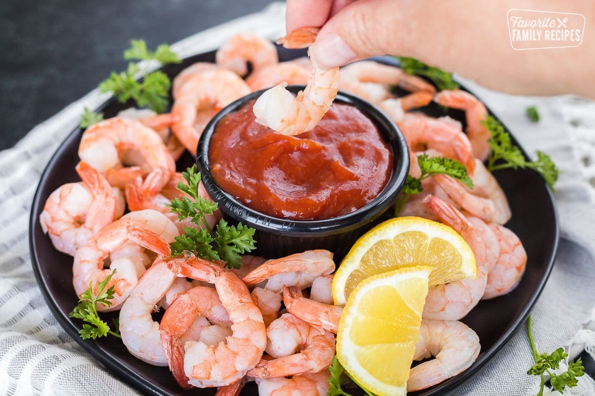 Shrimp being dipped into a bowl of homemade cocktail sauce.