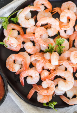 A platter of cocktail shrimp next to a cup of cocktail sauce