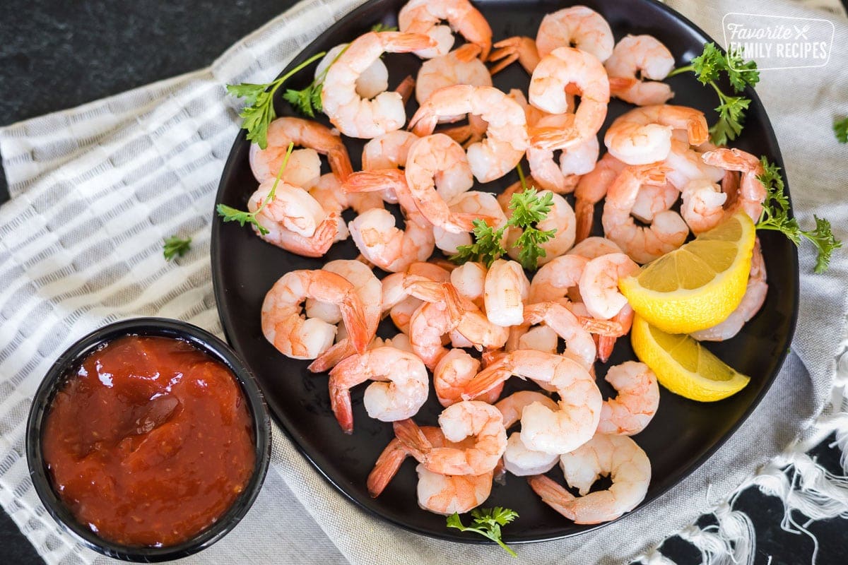 A platter of cocktail shrimp next to a cup of cocktail sauce.