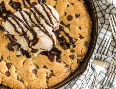 A large chocolate chip cookie baked in a cast iron skillet and topped with ice cream and chocolate sauce