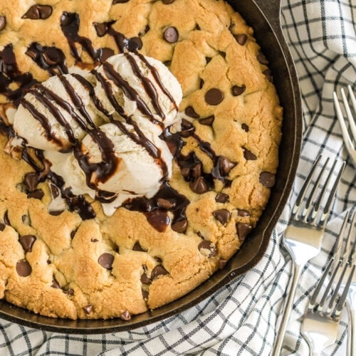 A large chocolate chip cookie baked in a cast iron skillet and topped with ice cream and chocolate sauce