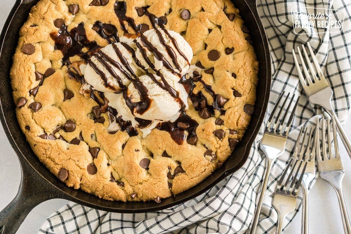 A large chocolate chip cookie baked in a cast iron skillet and topped with ice cream and chocolate sauce