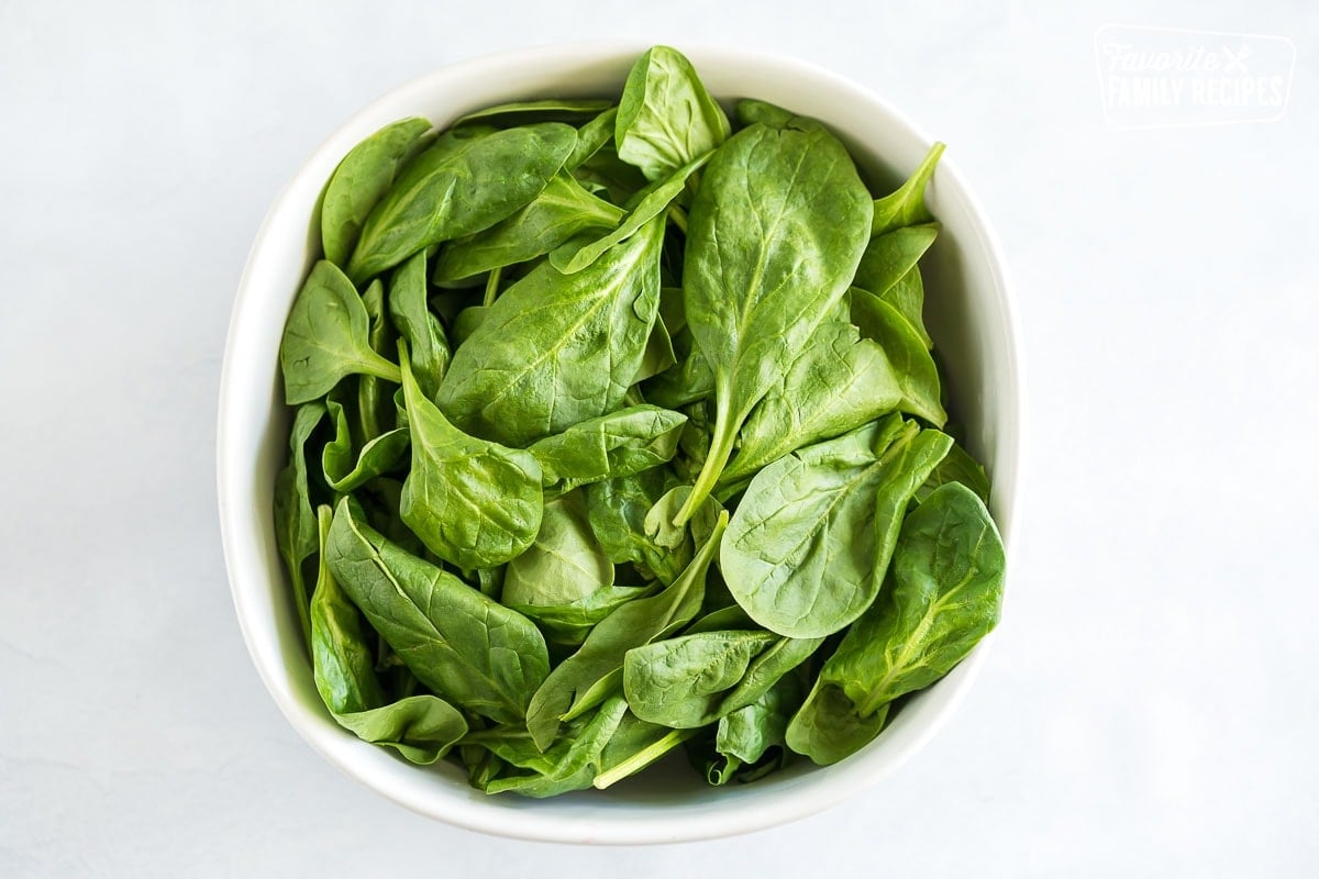 A large white serving bowl filled with spinach