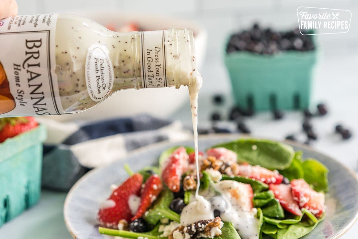 Poppyseed Dressing being poured on a Strawberry Spinach Salad.