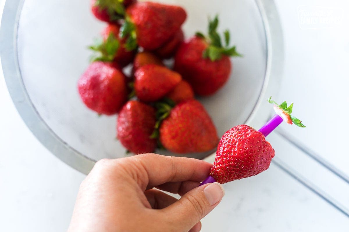 A straw being used to hull a strawberry