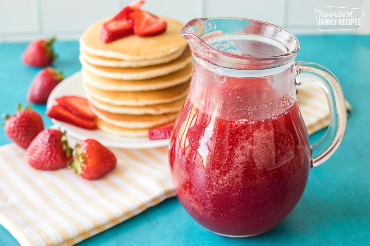 Strawberry syrup in a clear jar next to a stack of pancakes