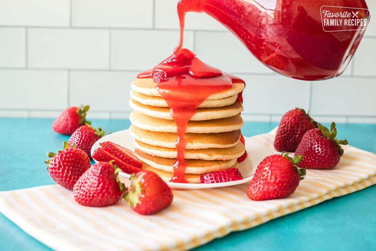 Strawberry syrup being poured over a large stack of pancakes