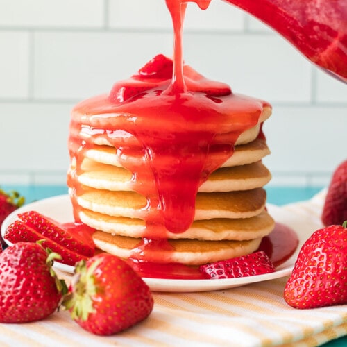 Strawberry syrup being poured over a large stack of pancakes
