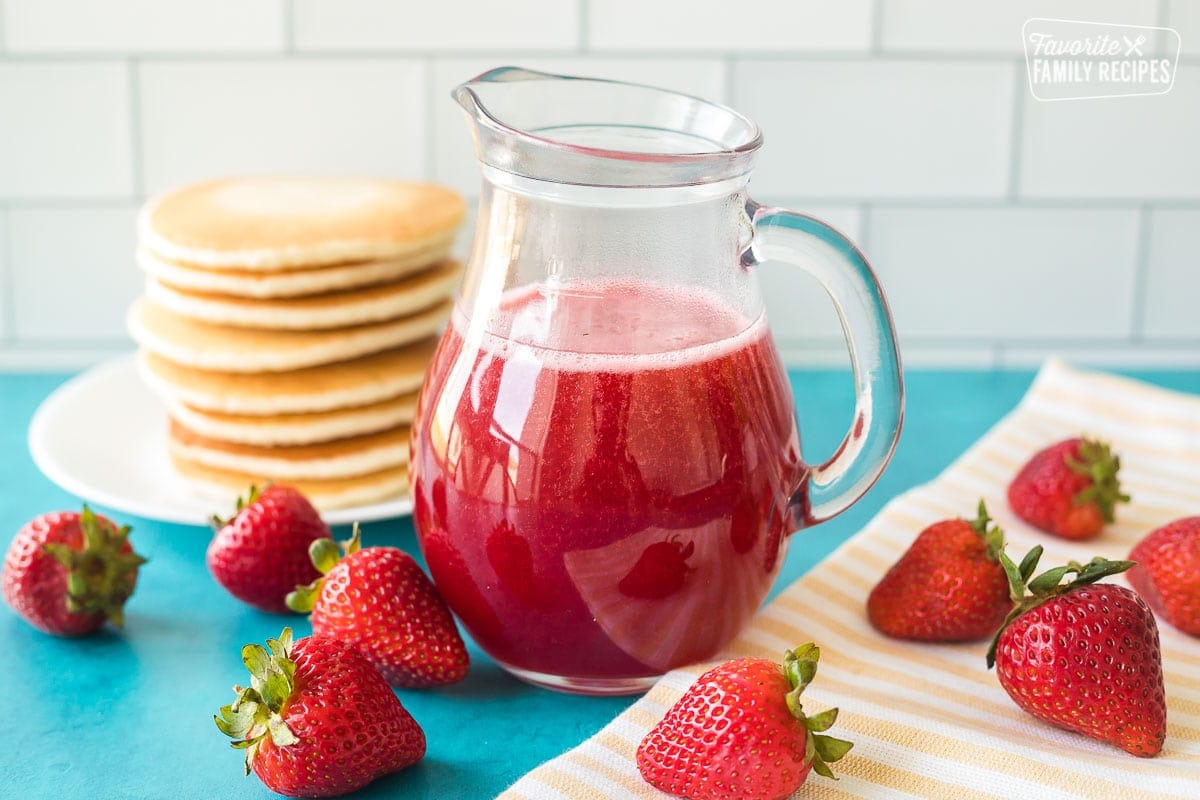 Strawberry syrup in a clear syrup jar next to a stack of pancakes