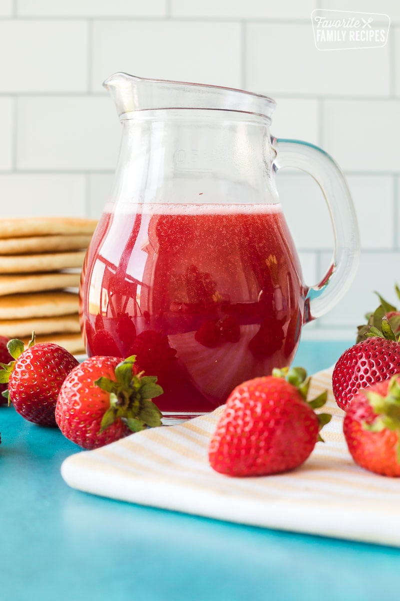 Strawberry syrup in a clear syrup jar.