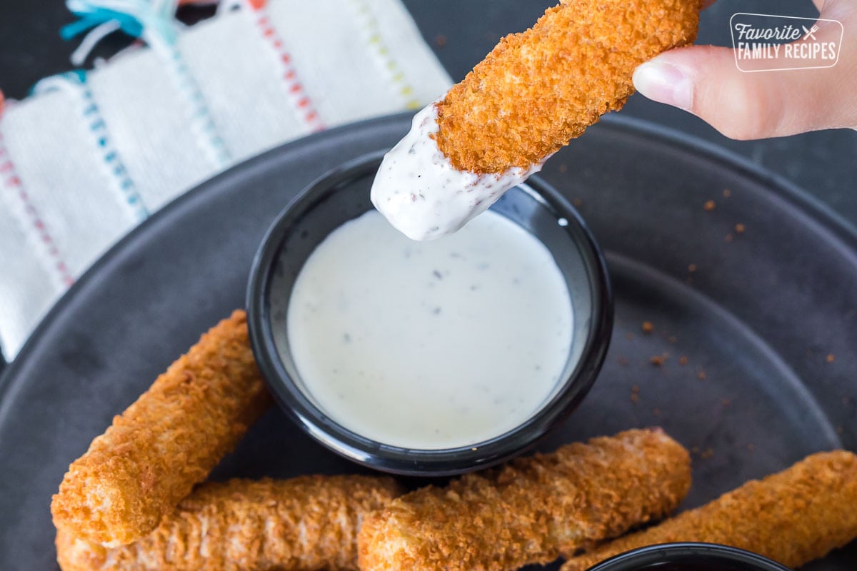 An air fried mozzarella sticks being dipped in ranch dressing