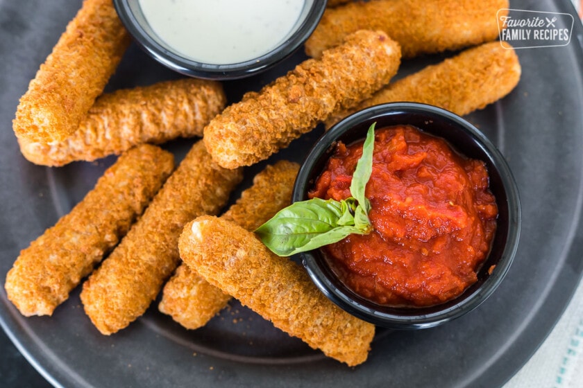 A close up of marinara sauce on a plate with mozzarella sticks