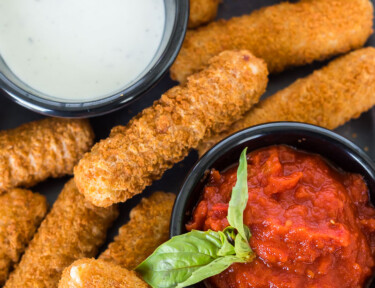 Air fryer frozen mozzarella sticks on a plate with dipping sauces