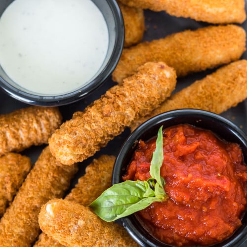 Air fryer frozen mozzarella sticks on a plate with dipping sauces
