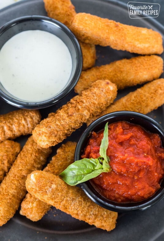 Air fryer frozen mozzarella sticks on a plate with dipping sauces