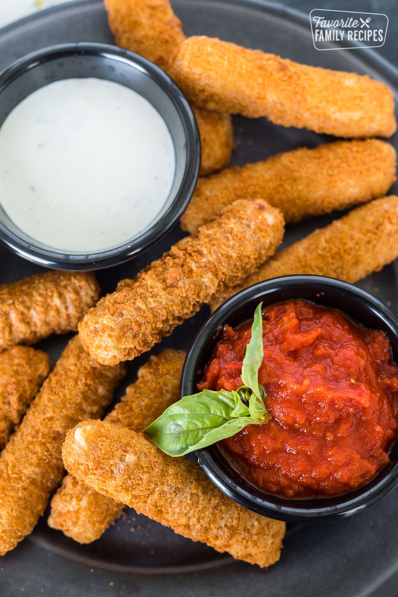 Air fryer frozen mozzarella sticks on a plate with dipping sauces