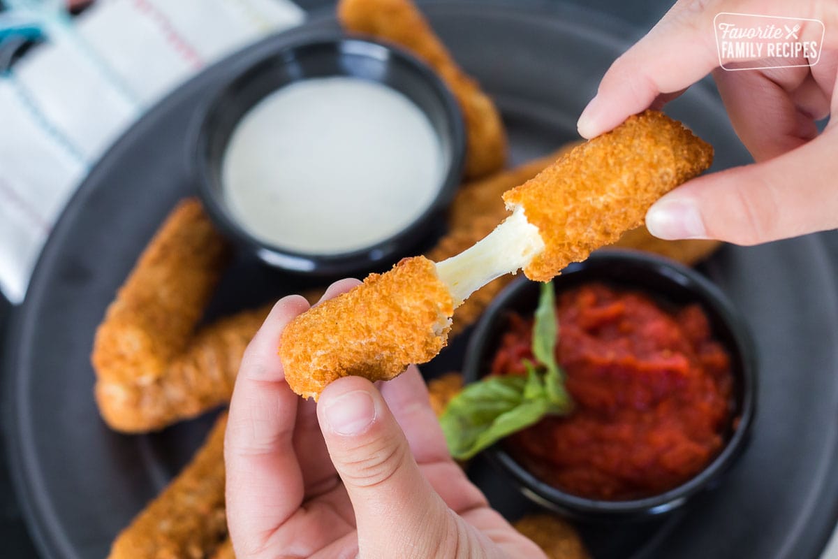 A mozzarella stick being pulled apart to show cheesy center.