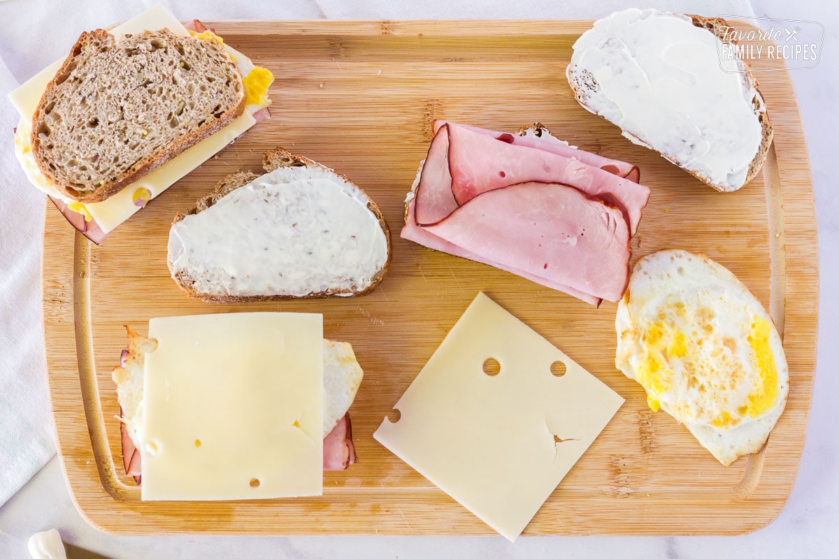 Cutting board with bread, ham, fried egg and Swiss cheese.