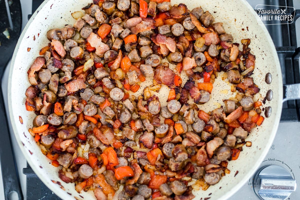 A large skillet with bacon, sausage, peppers, and onions to make breakfast tacos