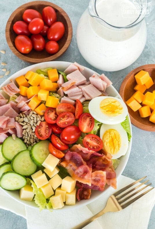 A chef salad topped with tomatoes, cheese, ham, bacon, and a hard boiled egg