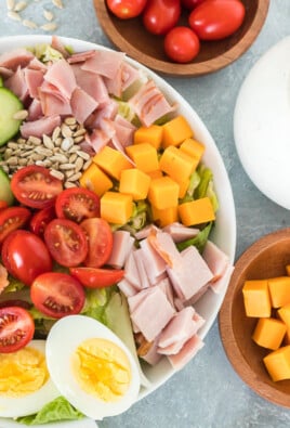 A chef salad topped with tomatoes, cheese, ham, bacon, and a hard boiled egg