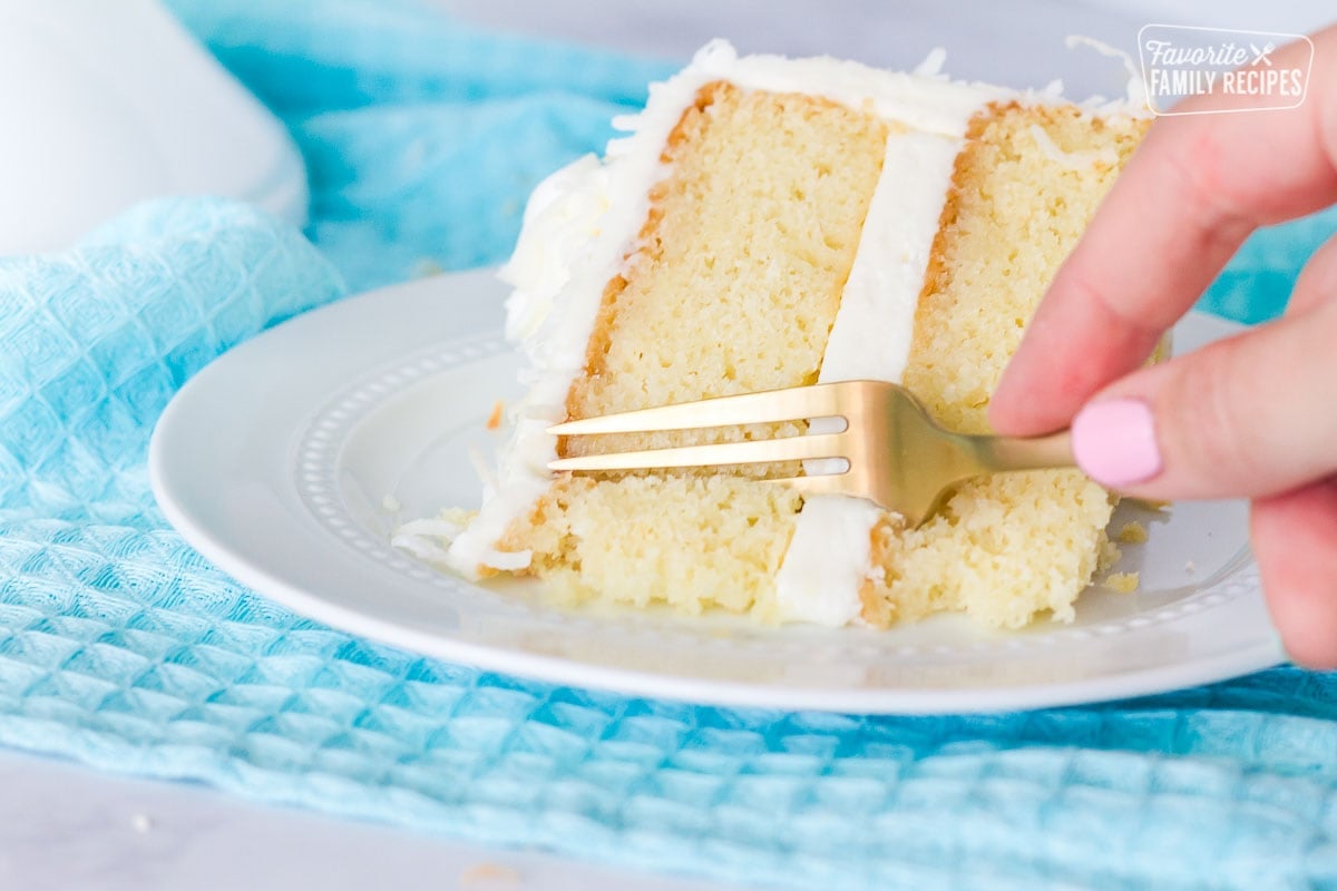 Fork cutting into a slice of coconut cream cake with coconut frosting.