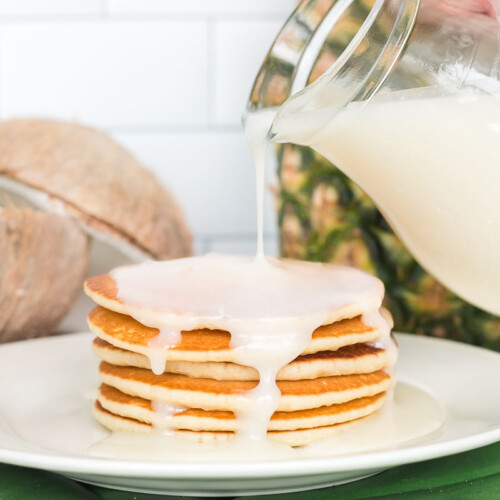 Coconut syrup being poured over a plate of pancakes