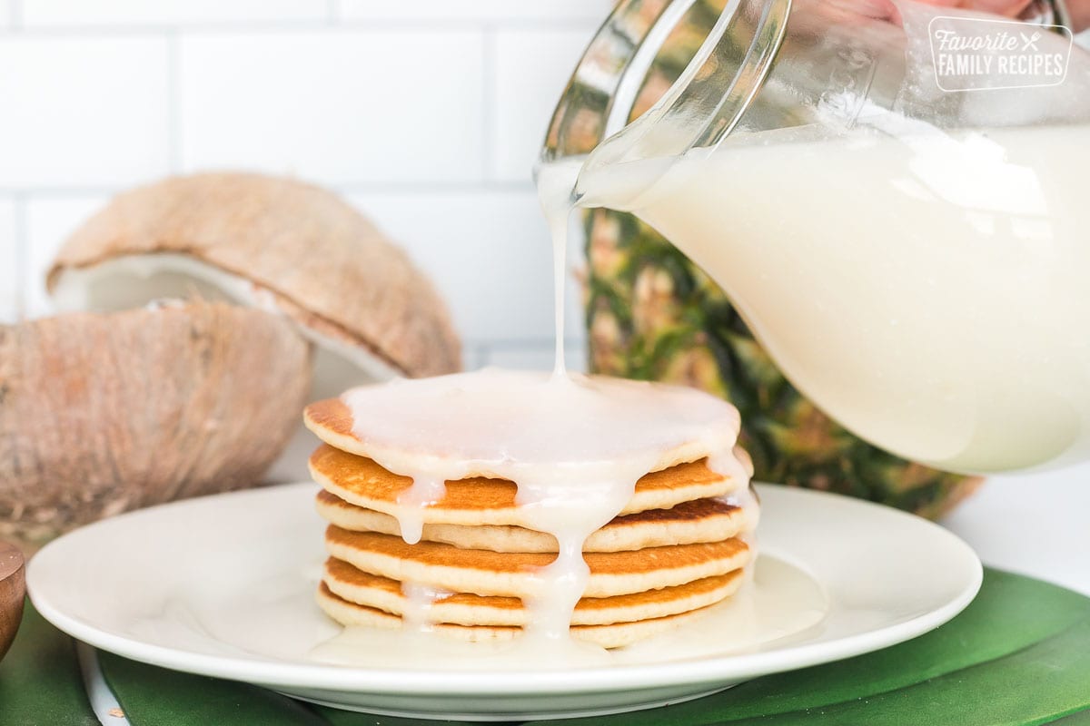 Coconut syrup being poured over a plate of pancakes