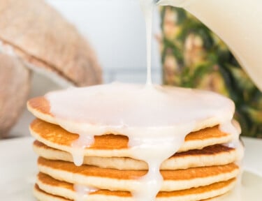 Coconut syrup being poured over a plate of pancakes