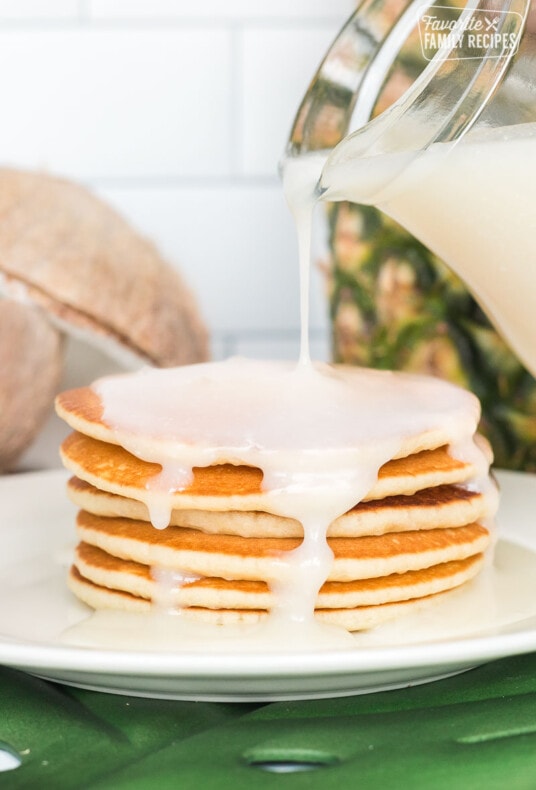 Coconut syrup being poured over a plate of pancakes