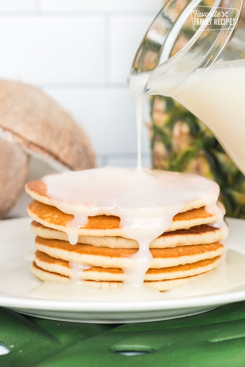 Coconut syrup being poured over a plate of pancakes
