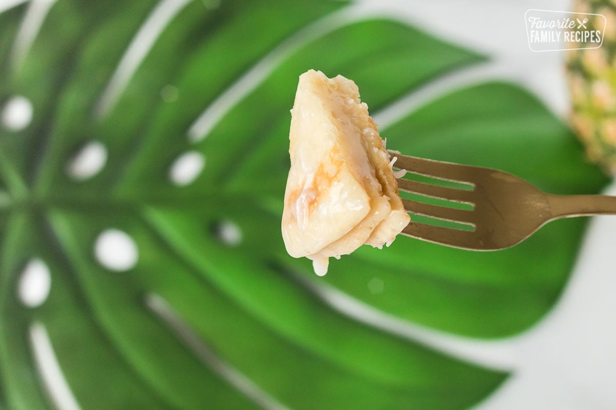 A close up of a bite of pancake on a fork with coconut syrup