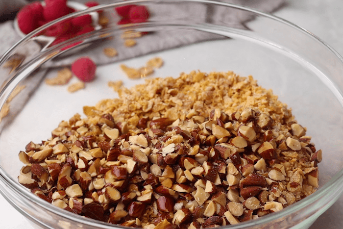 Crushed cereal, chopped almonds, and melted butter mixed in a bowl for Raspberry Fried Ice Cream.