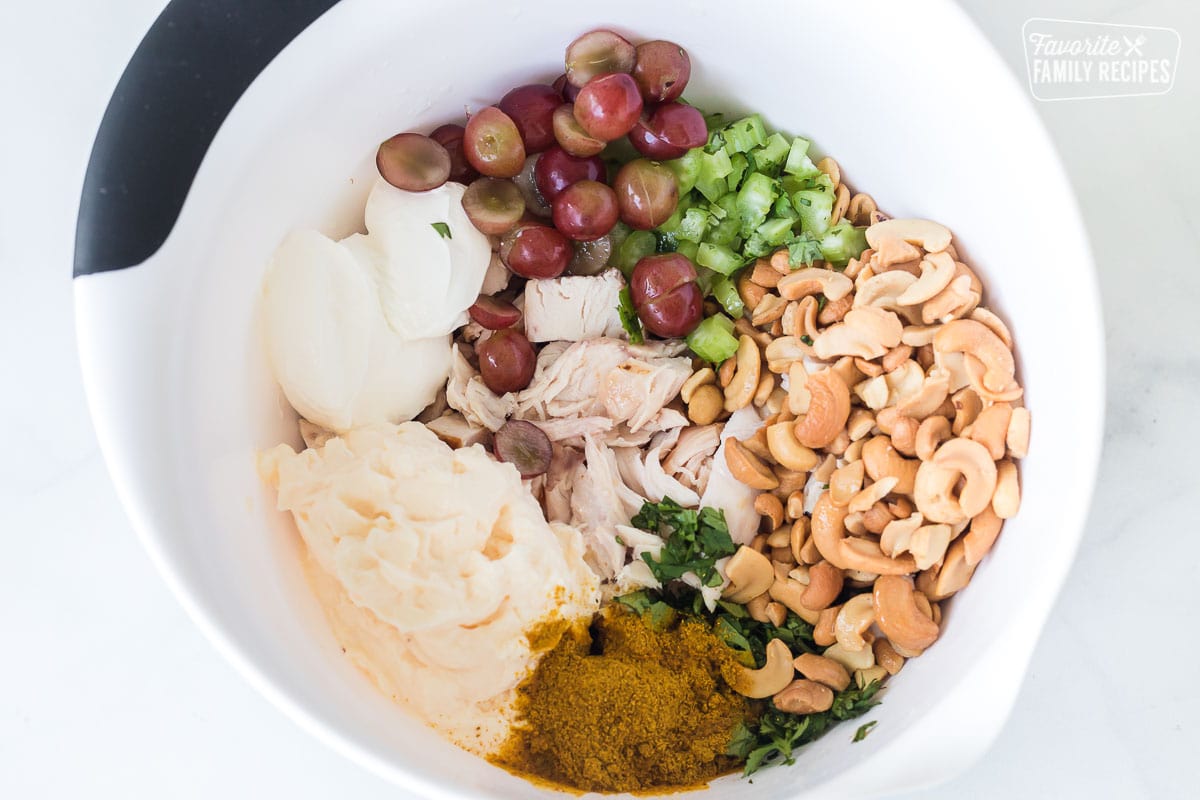 Ingredients to make curry chicken salad including chopped chicken, cashews, sauce, grapes, and celery.