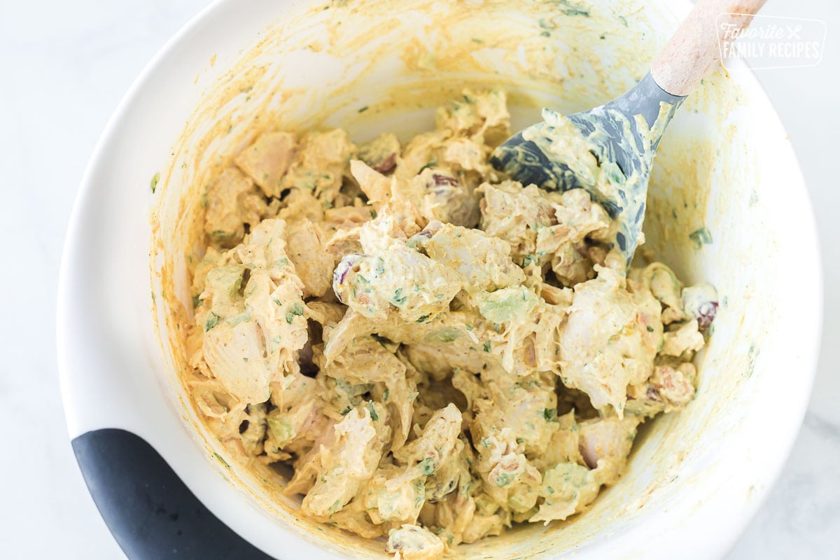 A mixing bowl of curry chicken salad being stirred