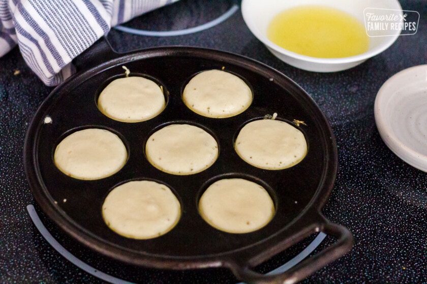 Danish Aebleskiver batter bubbled on edges in a pan.