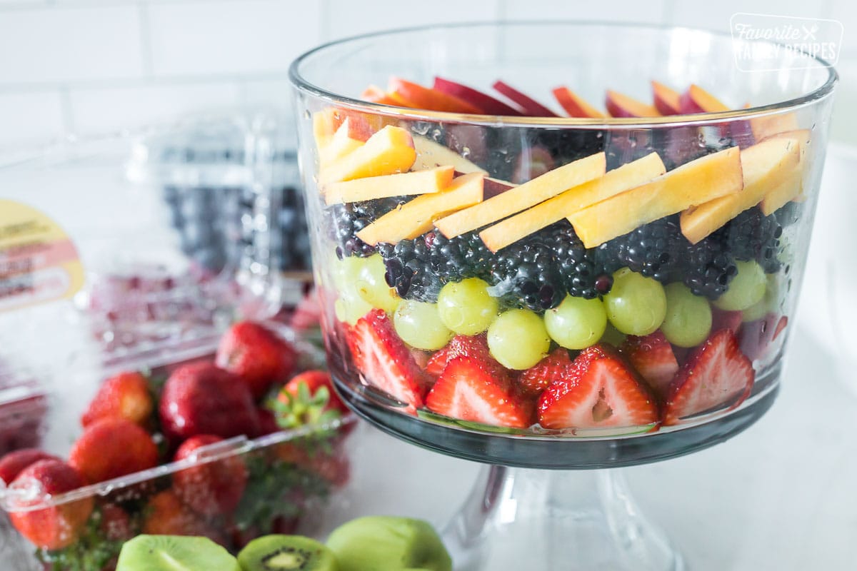 A fruit trifle being made with layers of strawberries, grapes, blackberries, and nectarines